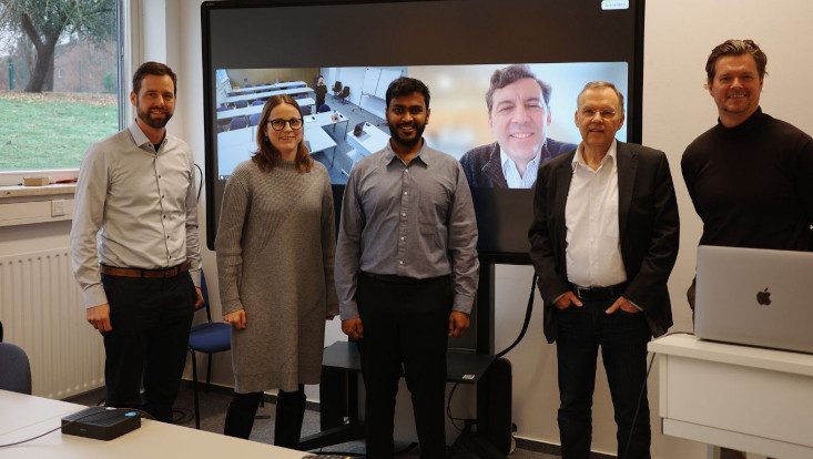 Group photo after the PhD defence, with the external reviewer joining by video on the screen behind.